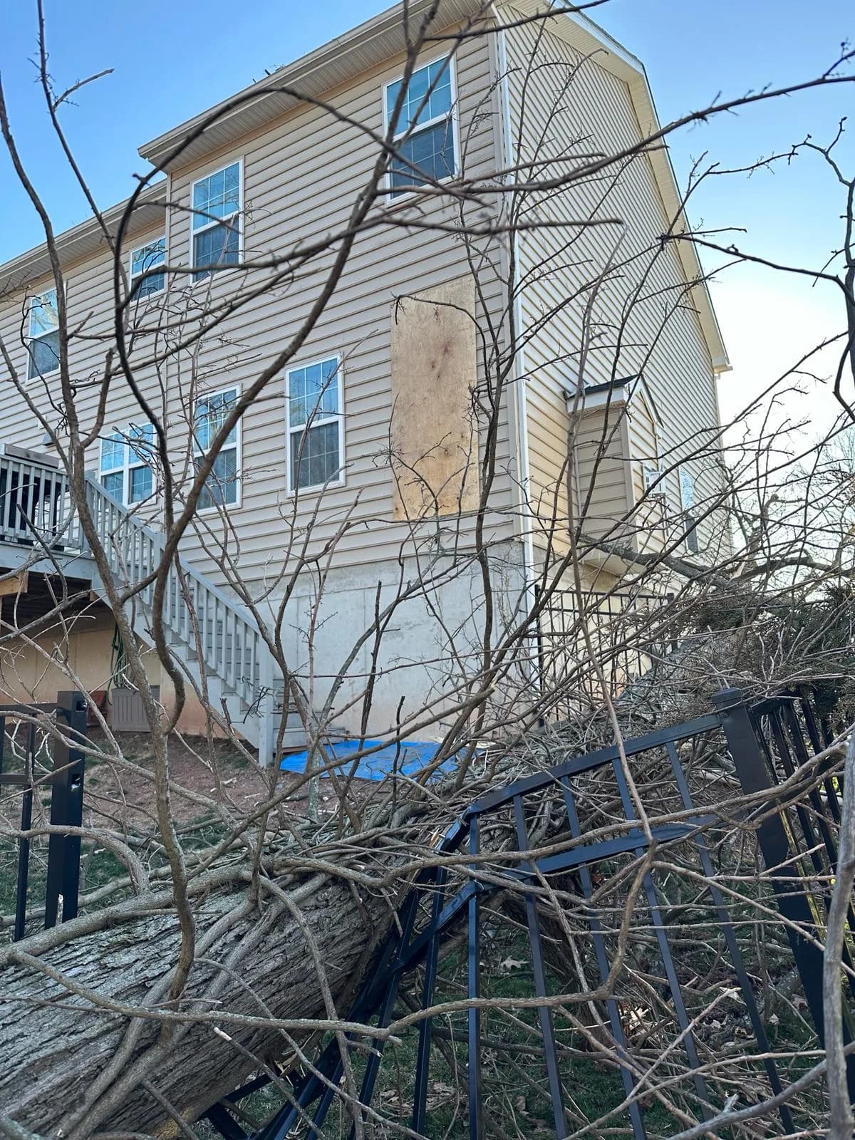 A fallen tree lying across a crushed fence against the side of a two-story house