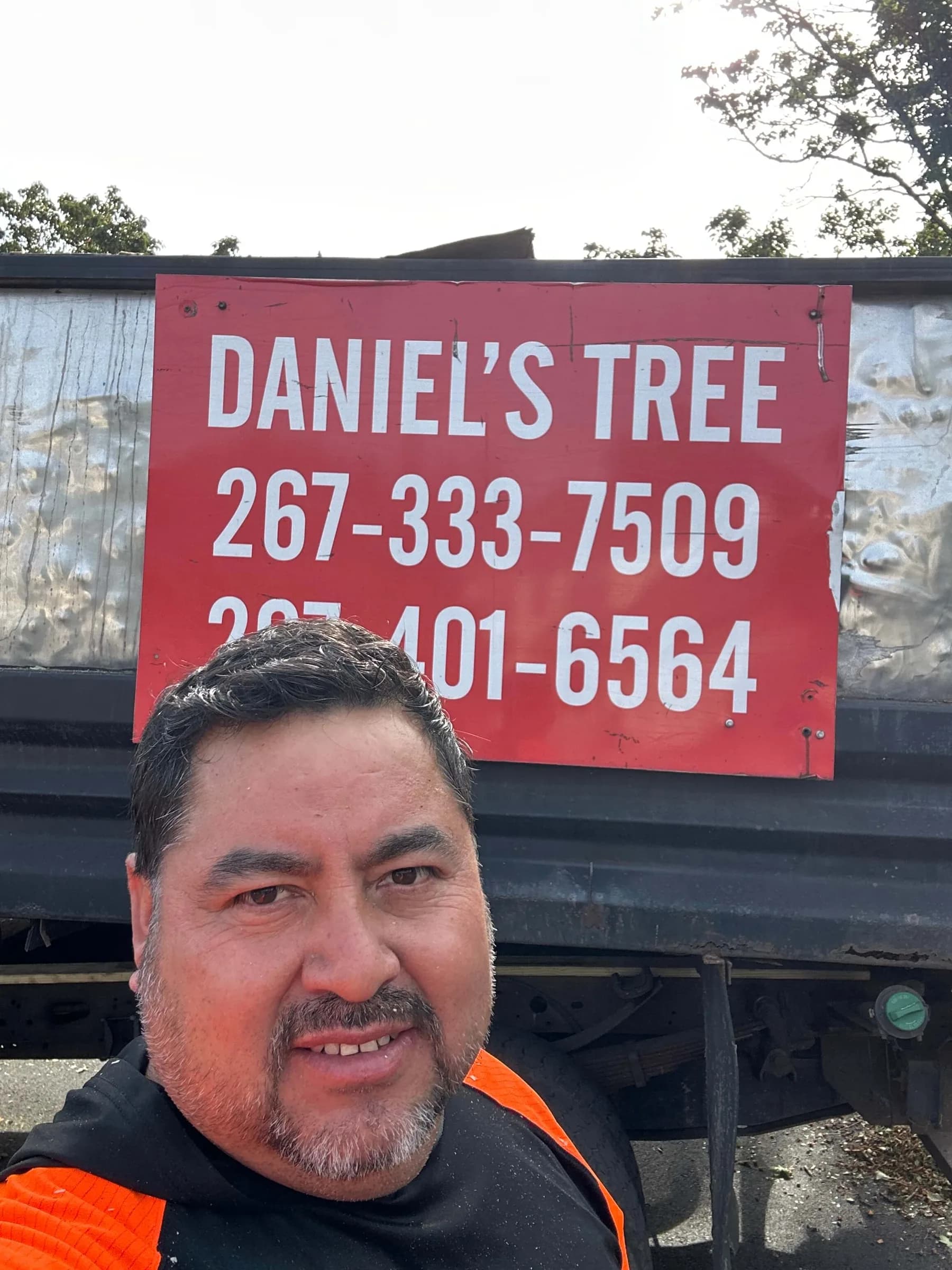 The owner of Daniels' Tree Service in a hi-vis work shirt, in front of the company truck and its sign