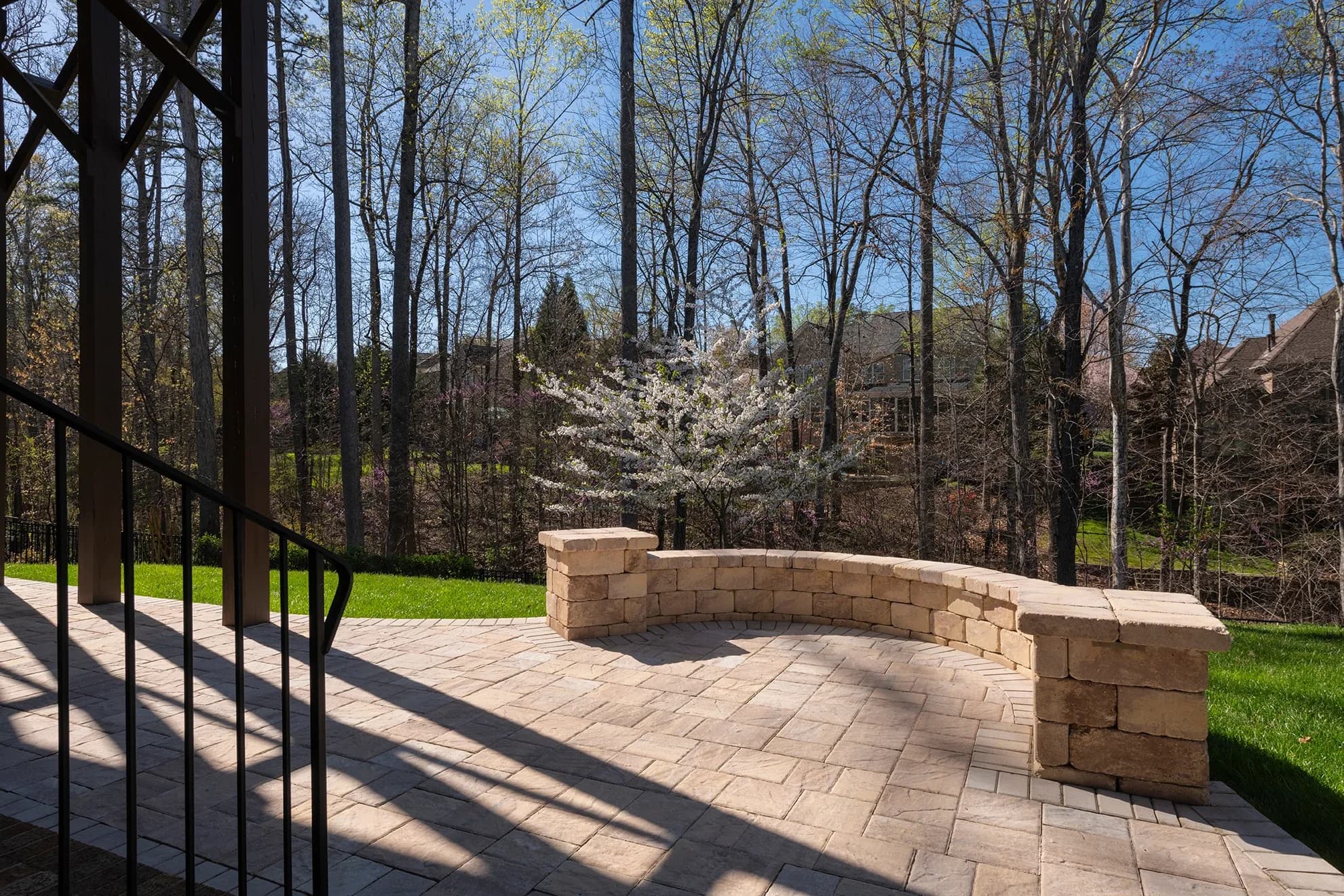 A paver patio with a curved stone seat wall, looking out to a wooded backyard