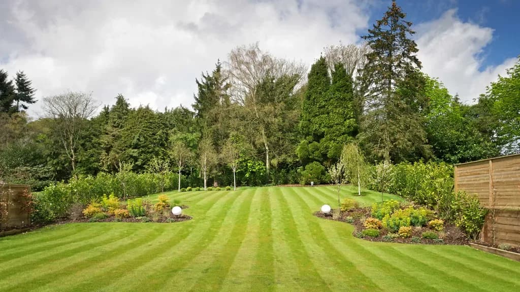 A freshly mown striped lawn edged with planted beds and backed by mature trees